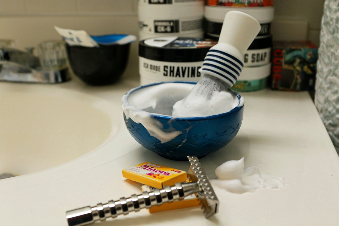 Shaving brush and bowl with lather and razor on sink