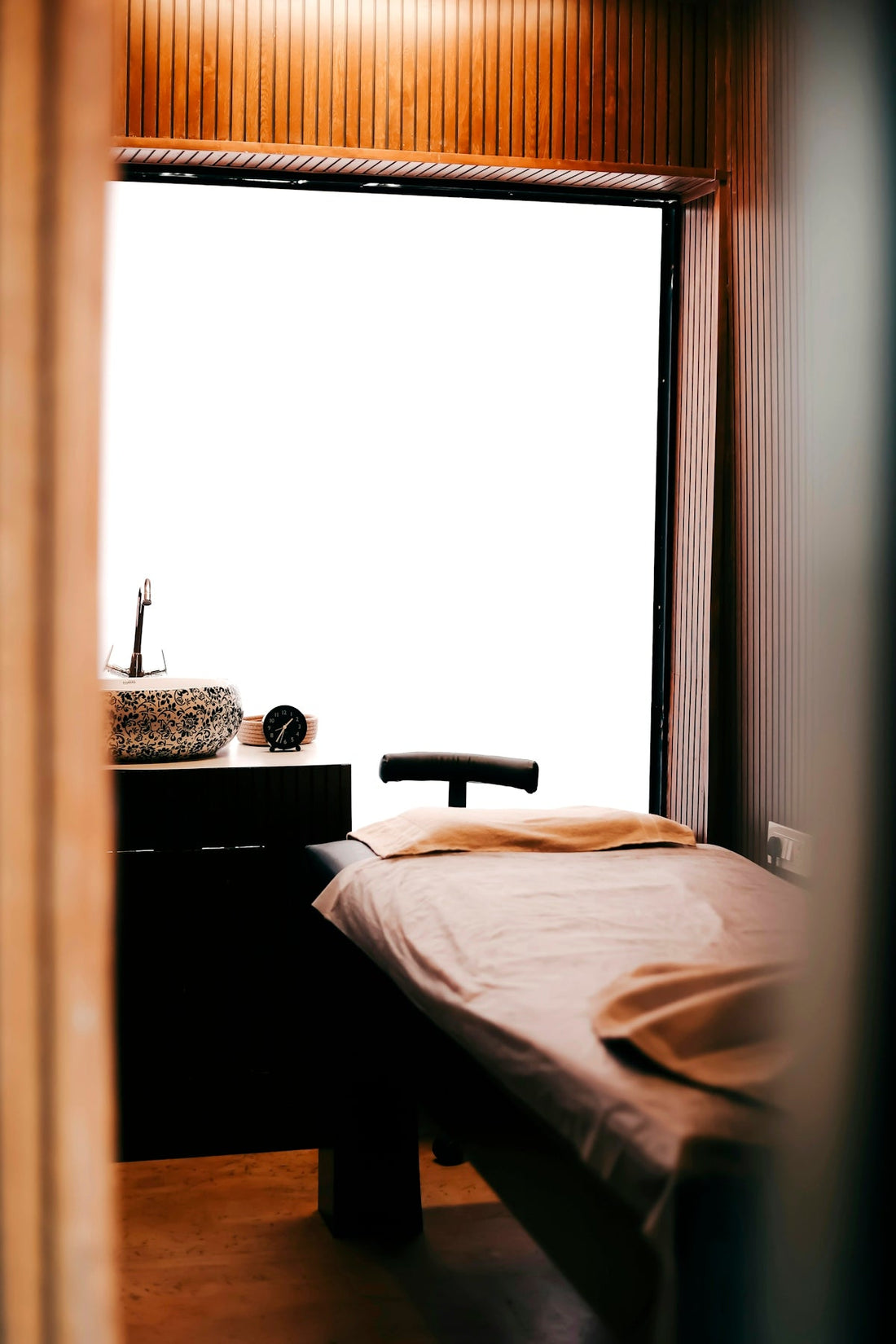 A massage table with a beige sheet beside a patterned sink in a spa